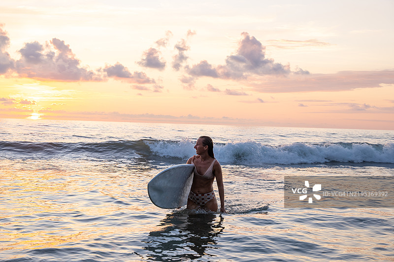 日落时分，冲浪女郎在海浪中漫步图片素材