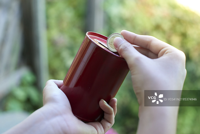 一个人把硬币放进红色储蓄罐里以储蓄。图片素材