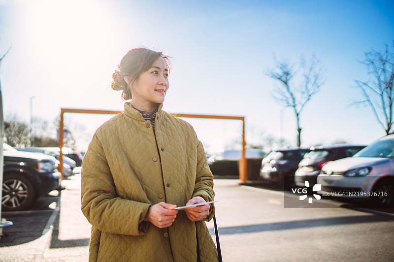 在阳光明媚的停车场里，女人手里拿着购物清单。图片素材