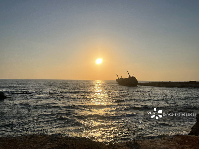 宁静海面上温柔波浪映衬下的金色日落前的船只残骸剪影图片素材