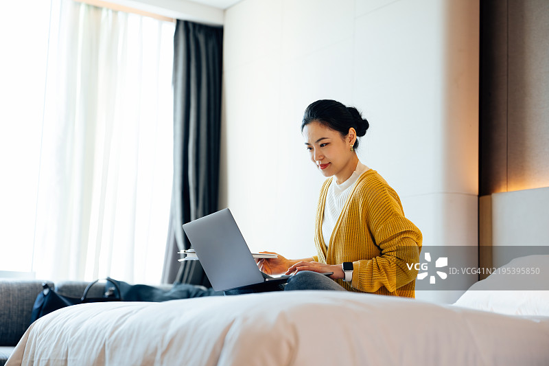 亚洲美丽女商人在酒店房间的床上使用笔记本电脑。商务旅行。图片素材