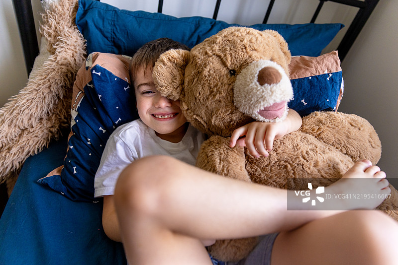 小男孩在自己的卧室里和他的泰迪熊玩耍图片素材