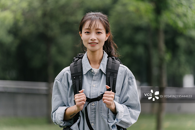 一个背着背包的女人站在一栋建筑前。建筑有很多玻璃窗，女人正看着它们。图片素材