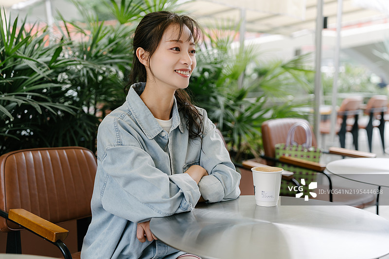 一位女士坐在桌子旁，手里拿着一杯咖啡。她面带微笑，享受着她的时光。图片素材