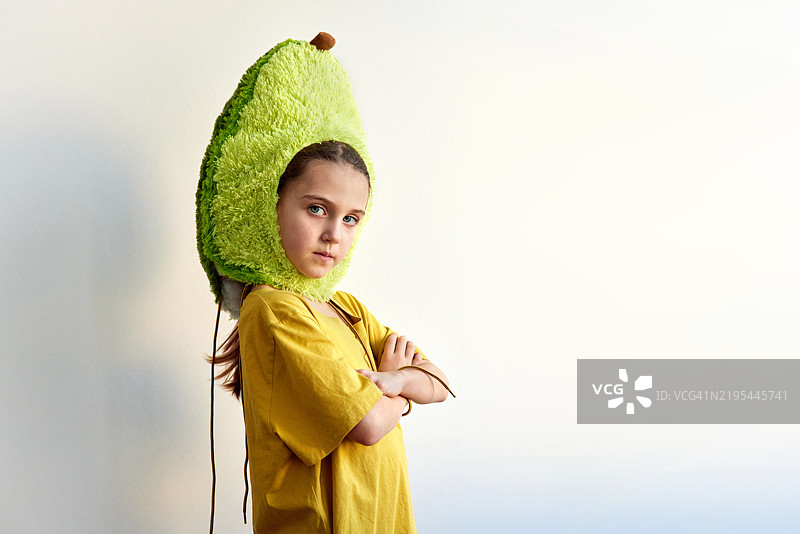 穿着鳄梨服装的小女孩双臂交叉，表情严肃。图片素材