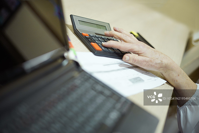 一只女性的手正在使用计算器和电脑进行计算图片素材