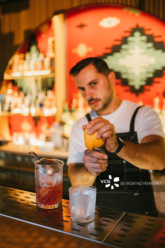 男性调酒师正在准备一杯橙皮尼格罗尼鸡尾酒。图片素材