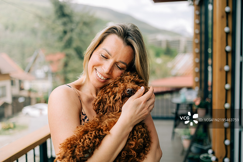 女人在阳台上拥抱她可爱的贵宾犬图片素材