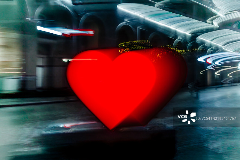 模糊城市景观中发光的红色心形象征着爱与亲情图片素材