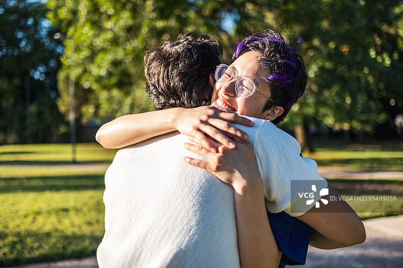 两个年轻朋友在明亮的公园环境中分享温暖的拥抱图片素材
