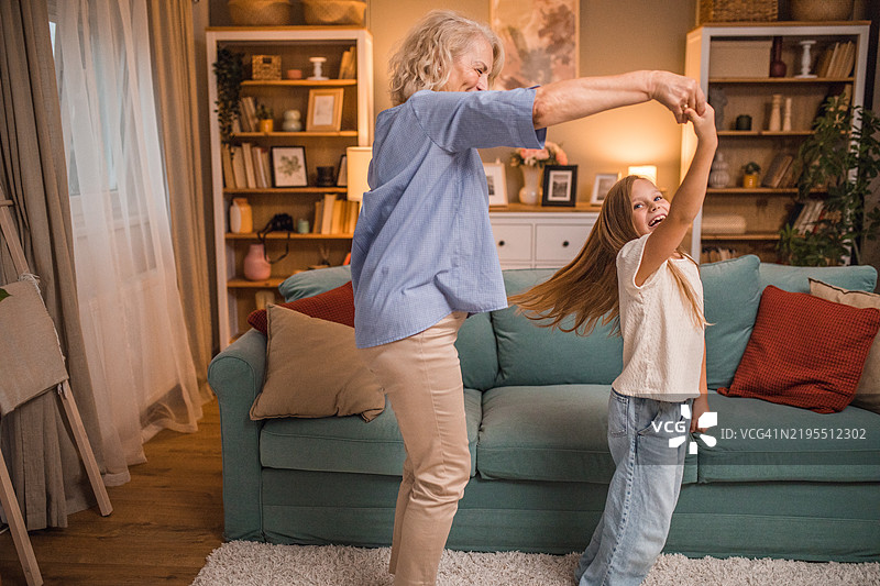 一个可爱的小女孩在客厅里和她无忧无虑的祖母一起享受舞蹈。图片素材