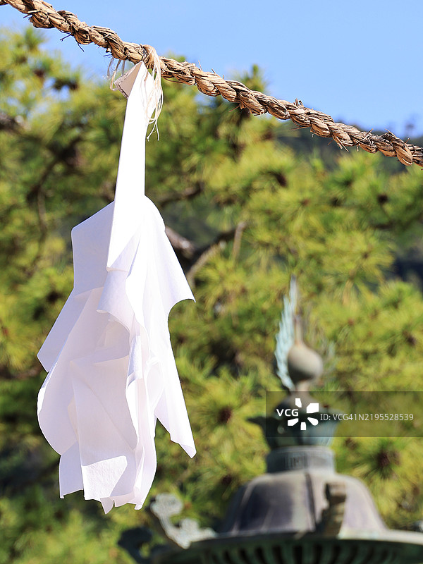 近距离拍摄悬挂在日本宫岛严岛神社的注连绳上的四手，旁边有金属灯笼。图片素材