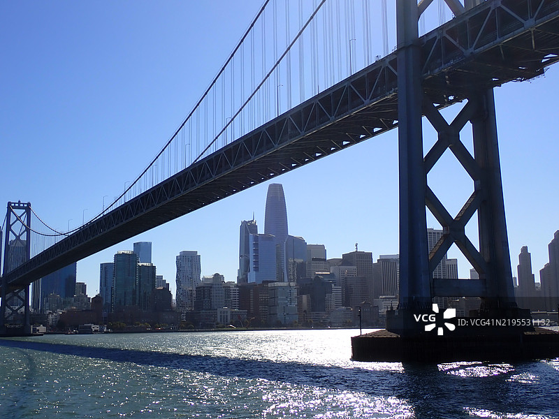 旧金山天际线在湾桥下，阳光明媚，水面上闪烁着光辉图片素材