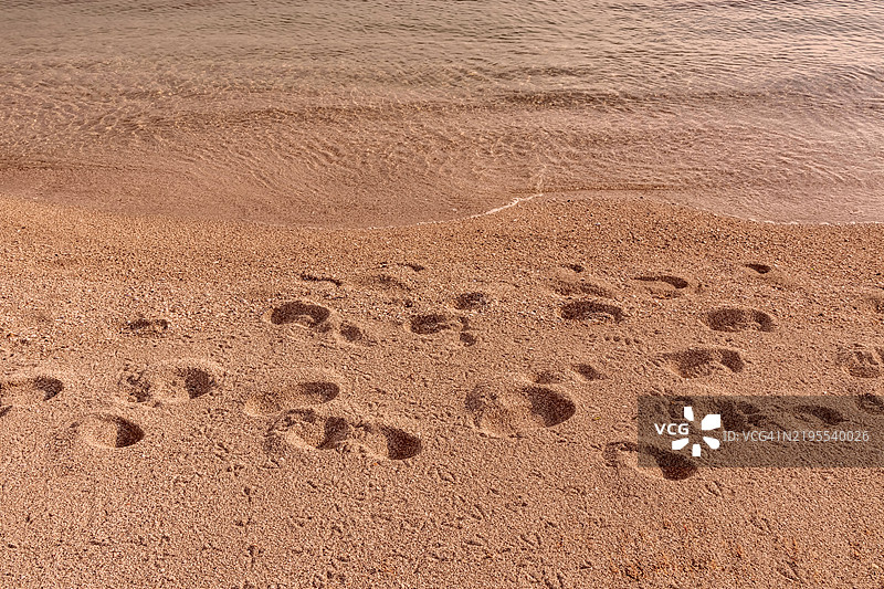 沙滩海岸上的脚印，温柔的海浪轻轻拍打着岸边图片素材