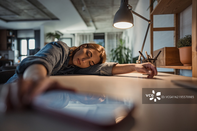 一位疲惫不堪的女性在桌子上睡着了。图片素材