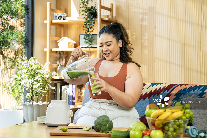 微笑的女性在温馨的家居环境中准备新鲜的绿色果汁图片素材