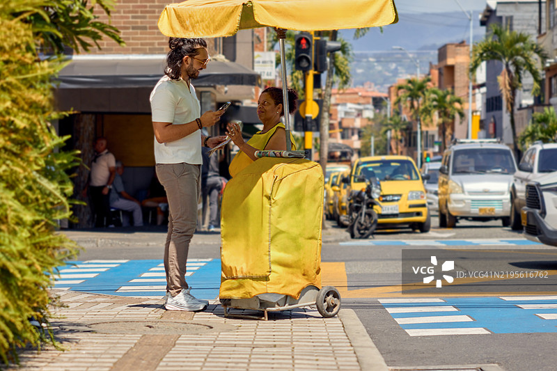 一名年轻男子用手机扫描街头报刊亭的二维码以支付报纸费用图片素材