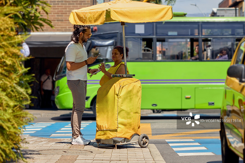 一名年轻男子用手机扫描街头报刊亭的二维码以支付报纸费用图片素材