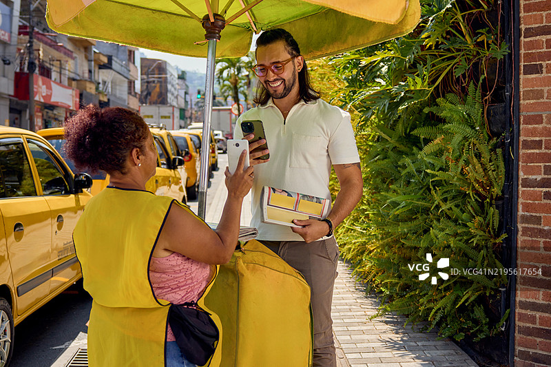 一名年轻男子用手机扫描街头报刊亭的二维码以支付报纸费用图片素材