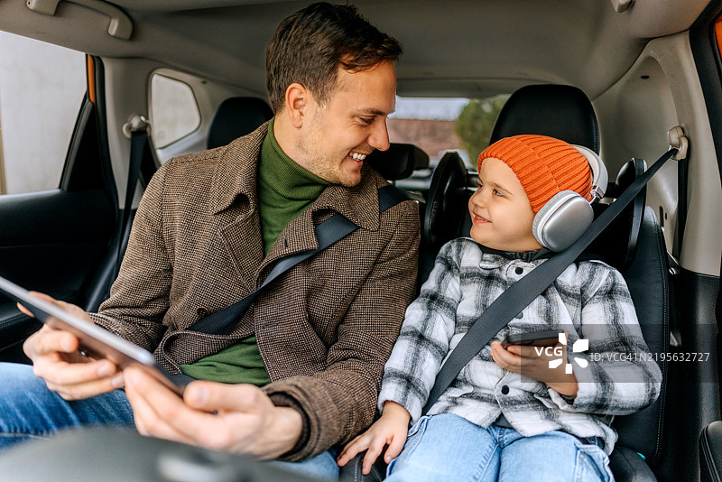 父亲和儿子在车后座上使用平板电脑图片素材