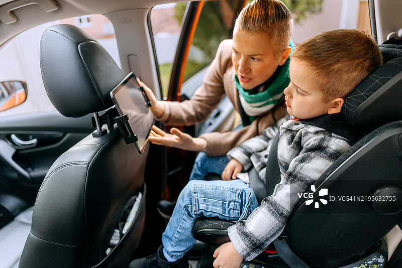 母亲在车座上为她的儿子设置平板电脑图片素材
