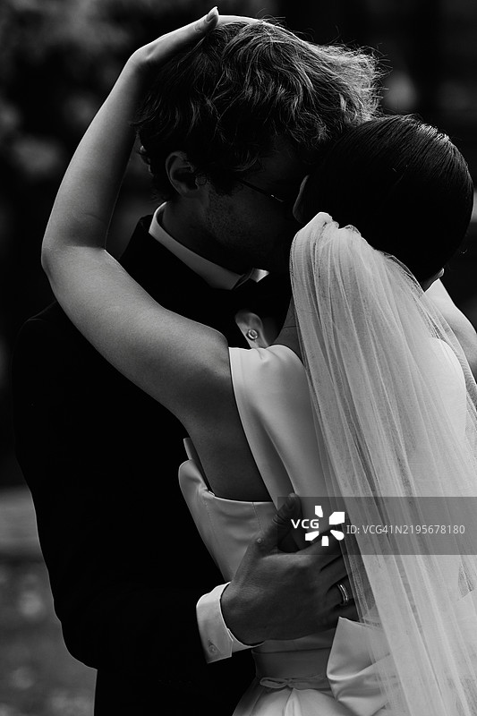 新婚夫妇在新娘的面纱下轻轻亲吻。一个感性的时刻。图片素材
