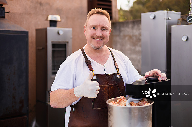 热情的爱好者在户外站在各种熏烤炉前，使用肉类搅拌机揉捏生肉，为香肠准备。图片素材