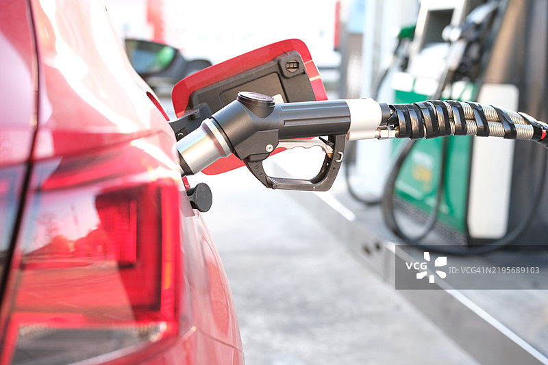红色汽车在加油站加油，背景是不断上涨的油价。能源危机与对石油的依赖 - 油价上涨图片素材