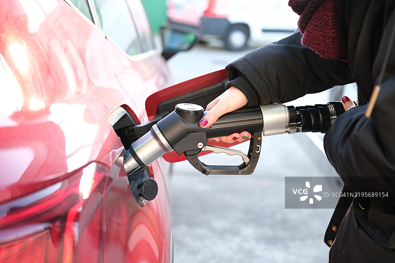 女性在加油站为红色汽车加油，背景是不断上涨的油价。能源危机与对石油的依赖 - 油价上涨 - 危机图片素材