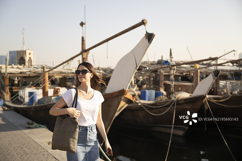 独自女性旅行者在迪拜溪边探索传统的阿拉伯帆船图片素材