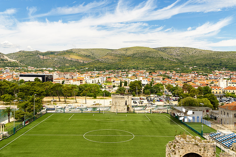 克罗地亚特罗吉尔的足球场高空视角，背景是小镇和山脉，蓝天晴朗。图片素材
