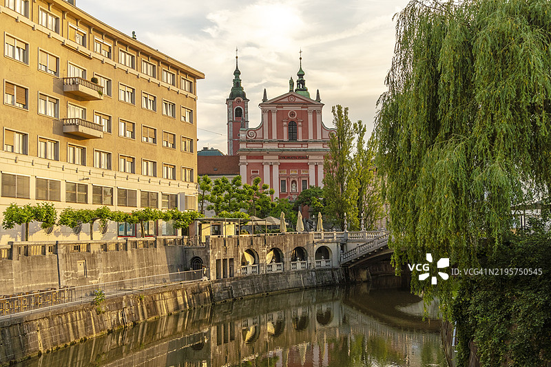 日落时分，宁静的河流穿过城市，背景是历史建筑和斯洛文尼亚卢布尔雅那的圣母领报方济各教堂。图片素材