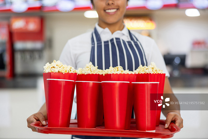 零售店员在电影院的售货亭里端着一盘小吃图片素材