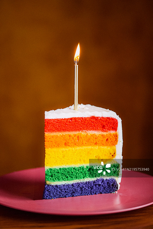 一片彩虹蛋糕，上面点缀着一根点燃的蜡烛图片素材
