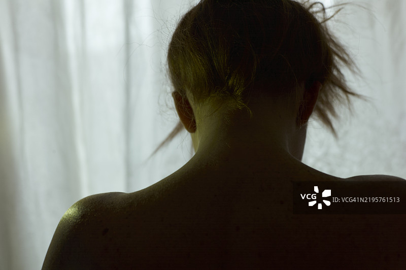 一位女性的剪影，头发盘起，背后是柔和灯光透过的薄纱窗帘。图片素材