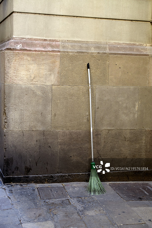 绿色扫帚靠在肮脏的米色墙壁上，旁边是混凝土人行道图片素材