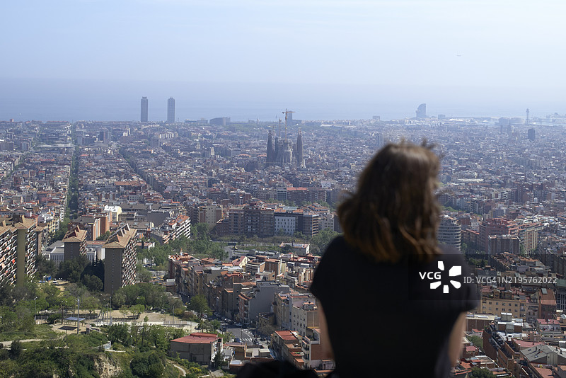 一位女性凝视着广阔的城市景观，远处有显著的建筑和海岸线，西班牙巴塞罗那图片素材
