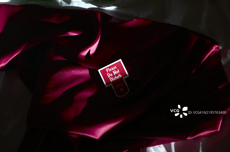 在美国新奥尔良的一间酒店房间内，红色丝绸长袍上挂着“请勿打扰”的门牌，在戏剧性的灯光下。图片素材