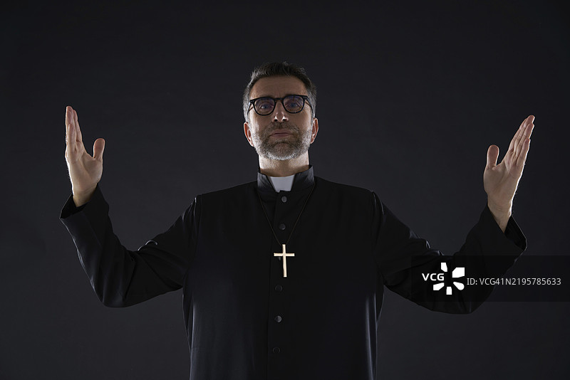 牧师张开双臂祝福，祈祷上帝，姿势孤立在黑色背景上图片素材