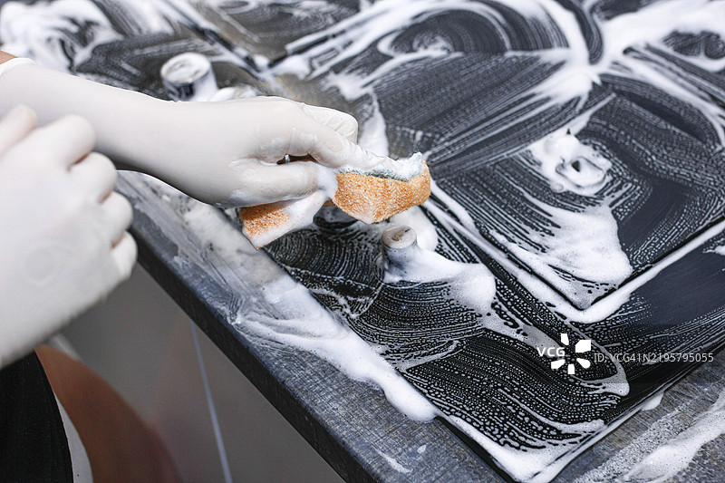 戴着手套的手用清洁刷清洗泡沫炉灶表面图片素材