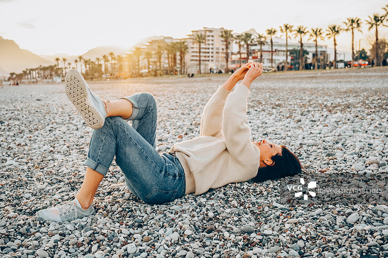 放松的年轻女性在日落时分享受卵石海滩的慵懒时光。图片素材
