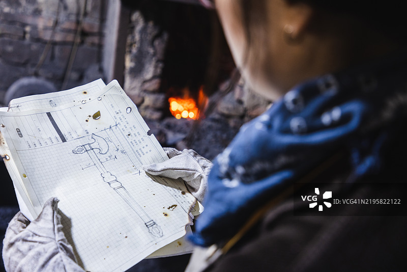 亚洲女性铁匠从背后看着金属艺术作品设计蓝图图片素材