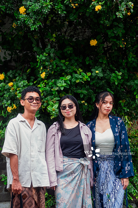 三位朋友穿着相同的爪哇服装在开花的树旁摆姿势图片素材