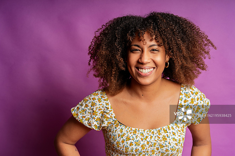 面带灿烂笑容的年轻女性，卷发，站在鲜艳的紫色背景前图片素材