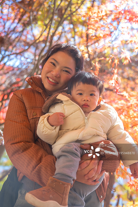 日本年轻女性微笑着与可爱的小男孩在樱花树下和湖边度过美丽的秋日，享受亲密的家庭时光。图片素材