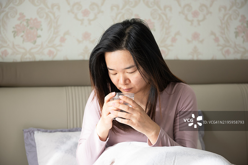 一位生病的女性正在喝一杯热水图片素材