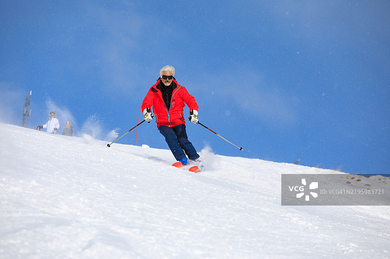 滑雪冬季运动。充满活力的男性滑雪者在阳光明媚的滑雪胜地享受滑雪的乐趣。大雪花在蓝天背景下飘落。图片素材