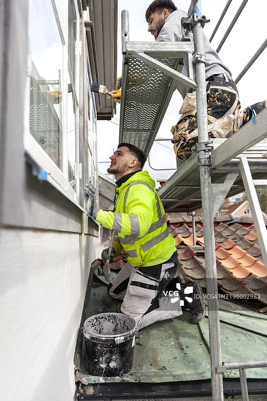 工人在房子外侧涂漆的侧面视图图片素材