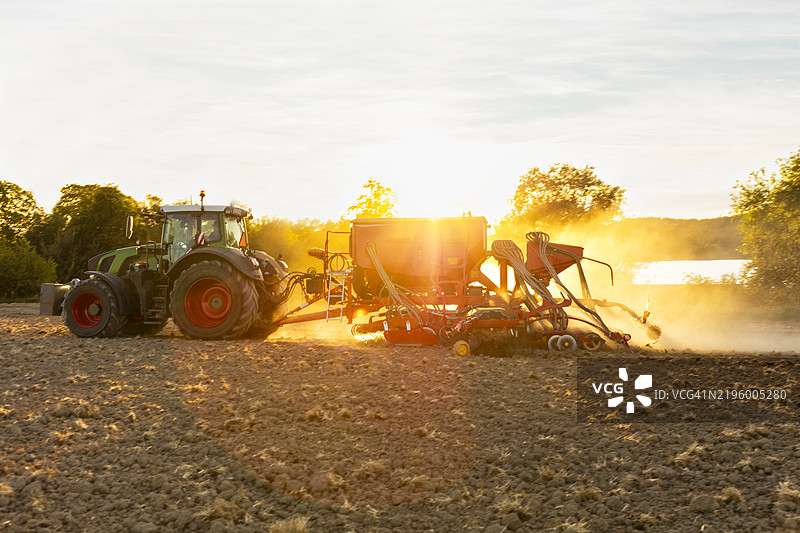 阳光明媚的日子里，拖拉机在田地里耕作，使用播种床耕耘机。图片素材