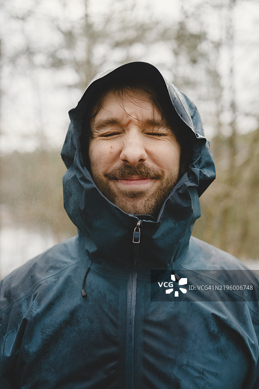 年轻男子穿着雨衣，闭着眼睛的特写镜头图片素材